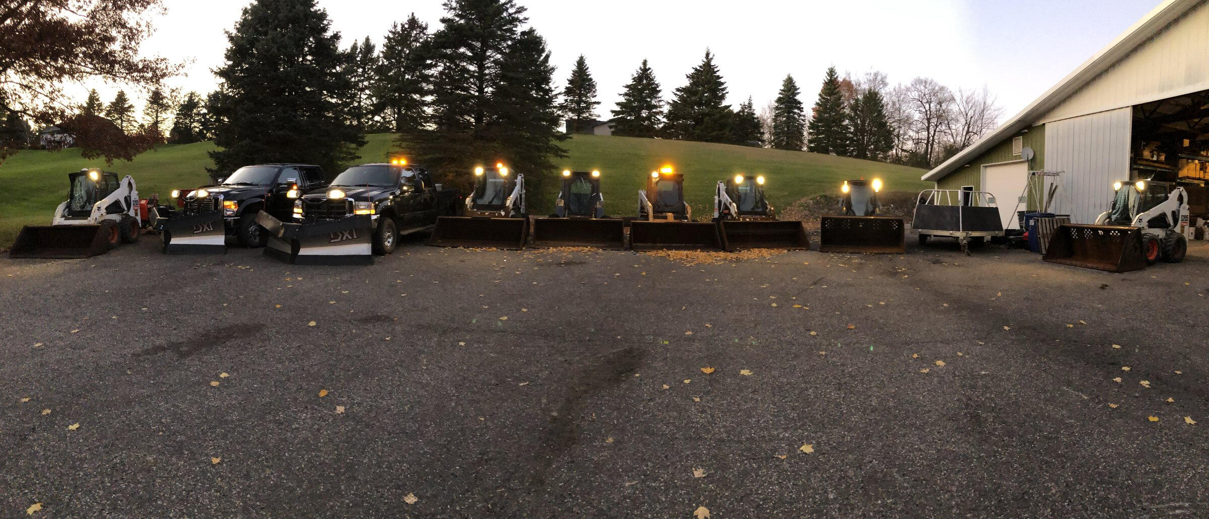 Fleet of plow trucks and skid steers lined up with lights on